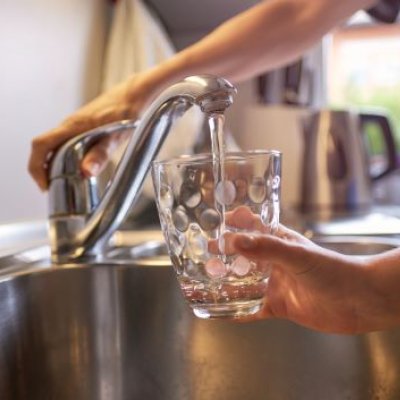 A close up a hand turning on a kitchen tap, filling a glass with water.